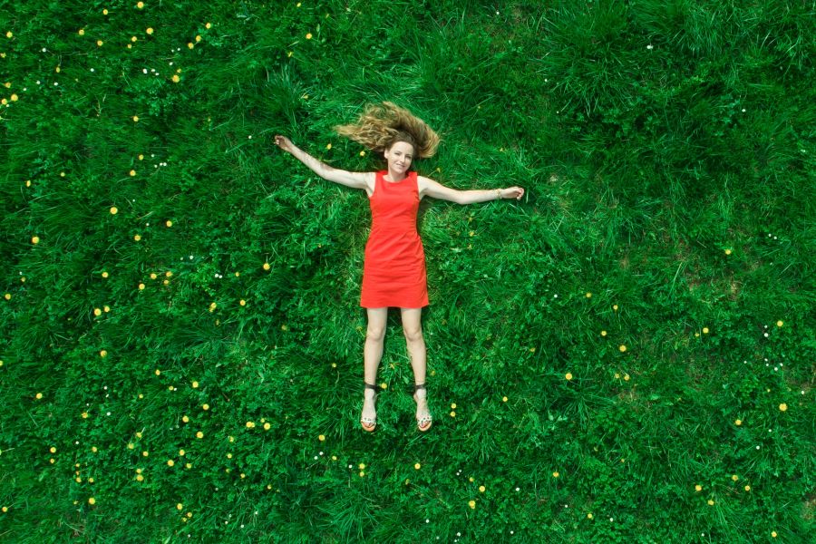 a girl in a red dress lying down in a bright green grassed field.