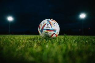 a soccer ball on a soccer pitch against the night sky and stadium lights