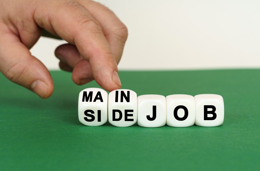 other work. cubes bearing the words main or side job on green and white background, with hand touching the cubes.