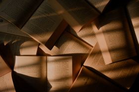 Patrick. Image is of a table filled with open books covered in shadows and strips of light.