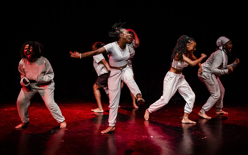 ‘FANGIRLS Residency and Response’. Photo: Herman Vewey. Stage dance performance with red lights and a dark background. Five dancers are doing energetic moves with their bodies on stage.