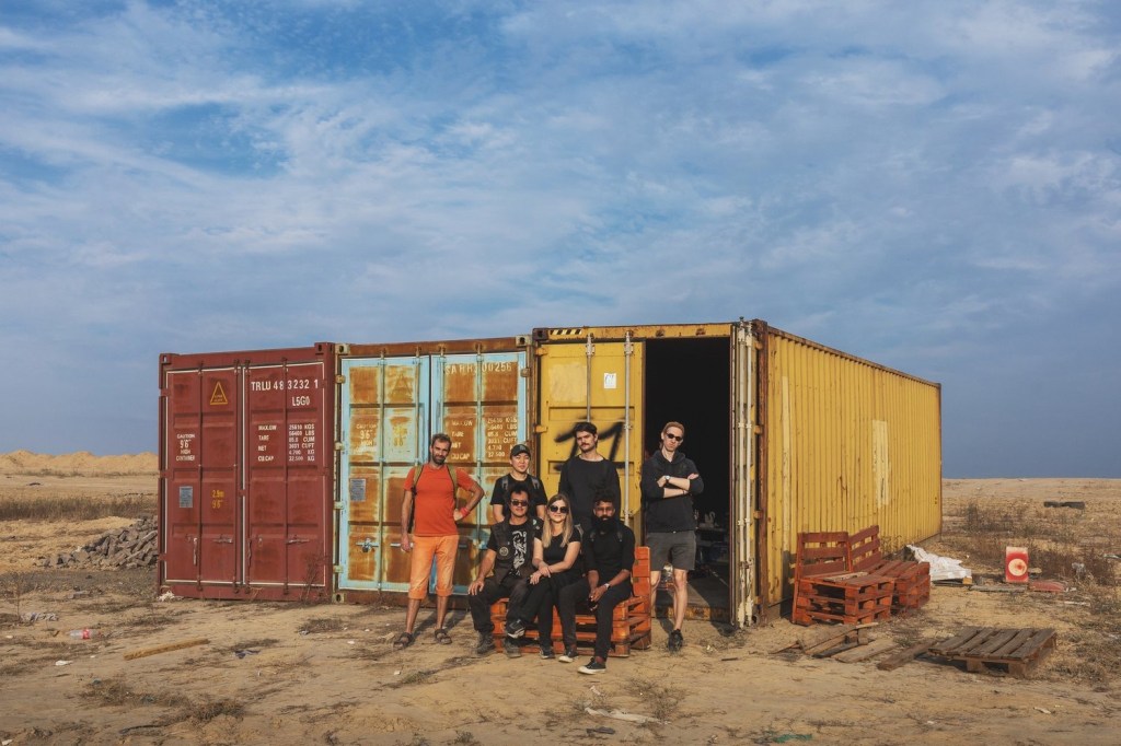 Trash Museum of Bishkek. Photo: Supplied. A shipping container in the middle of a desert landscape with seven people sitting and standing out the front.