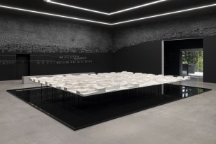 Installation in dark room with paper floating over a pool of water and chalk on walls. Archie Moore.