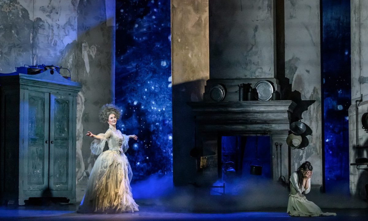 A fairy godmother on the left, in a resplendent gown. On the right is Cinderella, sitting with her head in her hands near the hearth of a fireplace.