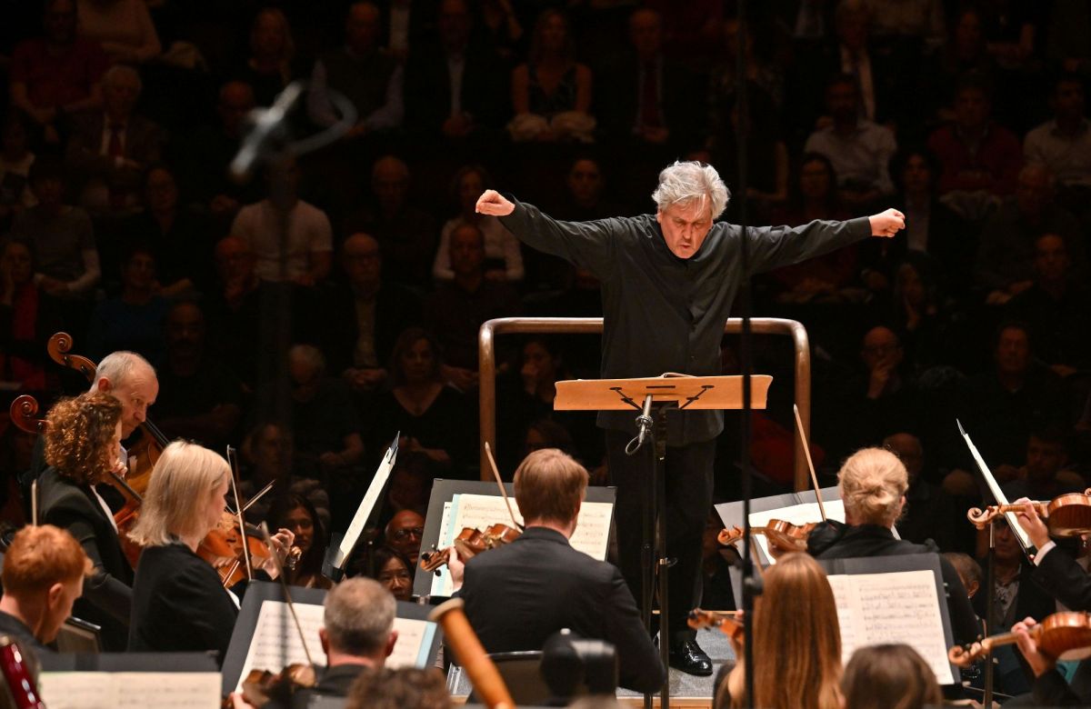 Sir Antonio Pappano conducts the London Symphony Orchestra. A grey-haired man, arms outstretched dramatically at shoulder height to either side, stands at a podium conducting an orchestra. His face is lined and he is dressed in black; the audience is visible behind him.