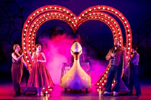 ENO's Così fan tutte plays the London Coliseum in February. Performers emote under a large, heart-shaped arch, through which a large swan-shaped vessel approaches.