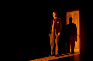 The Woman in Black 2025. An actor in Edwardian dress stands in a narrow strip of light, his back to a door and looking horrified.